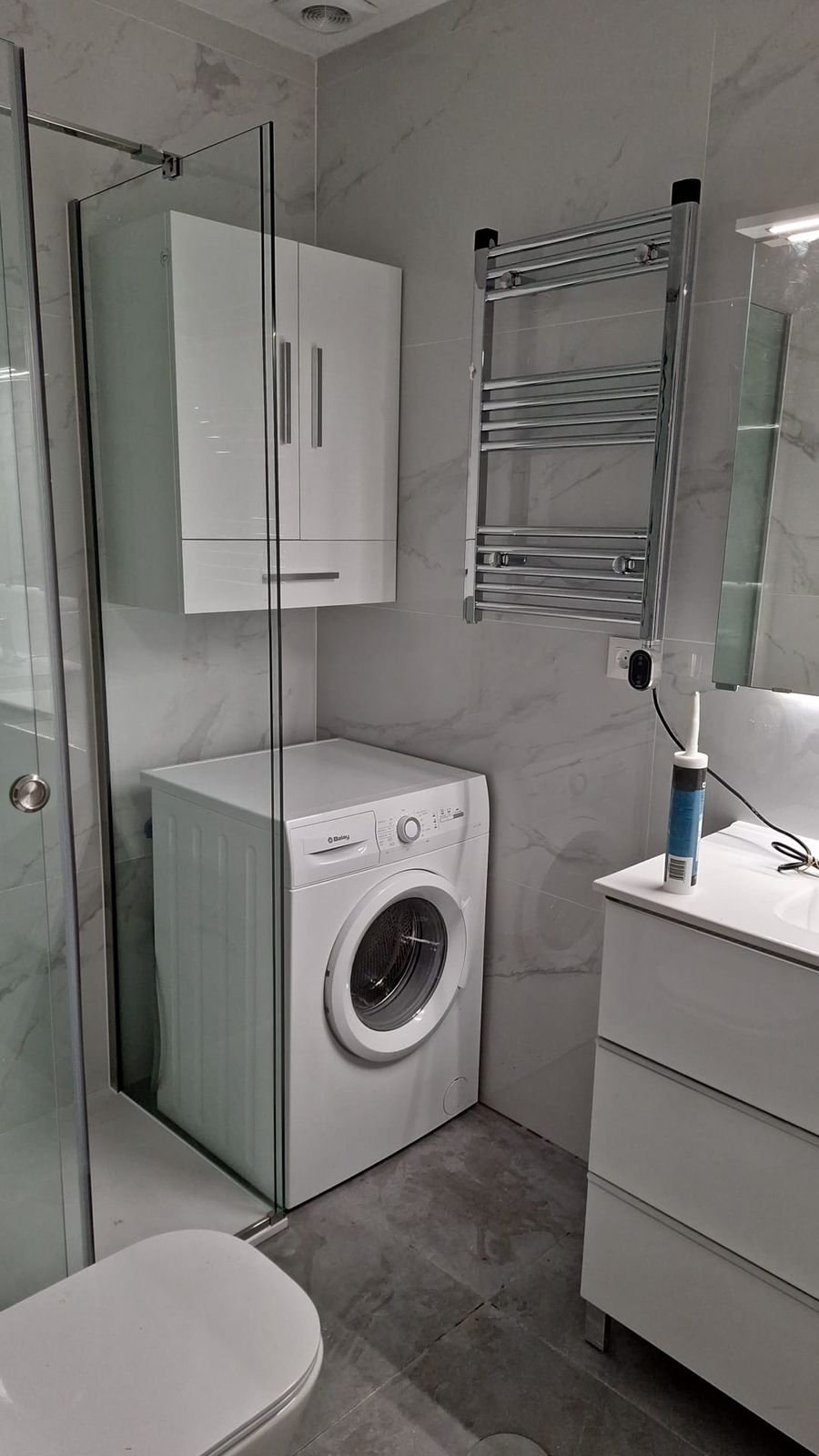 Baño reformado con ducha de cristal, toallero y mueble blanco