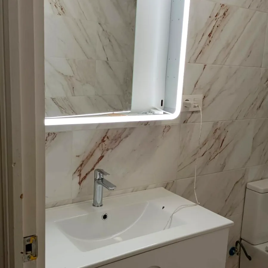 Espejo con luz LED y mueble de lavabo en un baño reformado